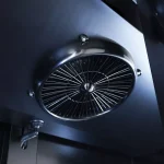 Circular metal ventilator/fan with radial blades mounted on a dark surface (ceiling)