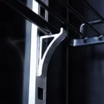 Close-up of a metal shelf support bracket attached to a vertical rail inside a dark cabinet.