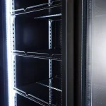 Empty upright glass-door refrigerated display case with wired shelves and bright interior LEDs.