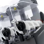 Close-up of a transparent safety shielded machine with two black clamps and white rotating parts; warning labels visible.