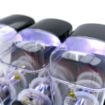 Close-up of three purple-tinted protective goggles with yellow warning labels and clear frames.