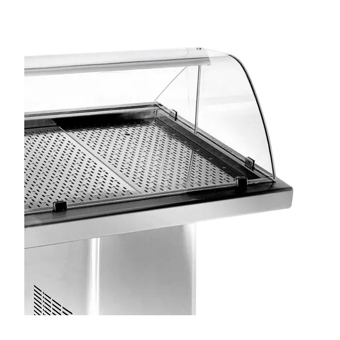 Stainless steel refrigerated display counter with a curved glass sneeze guard and perforated tray, empty for food display.